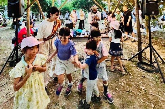 ながいけ認定こども園の夏祭りで、講師と園児たちが屋外のやぐらの前で一緒に踊っている様子